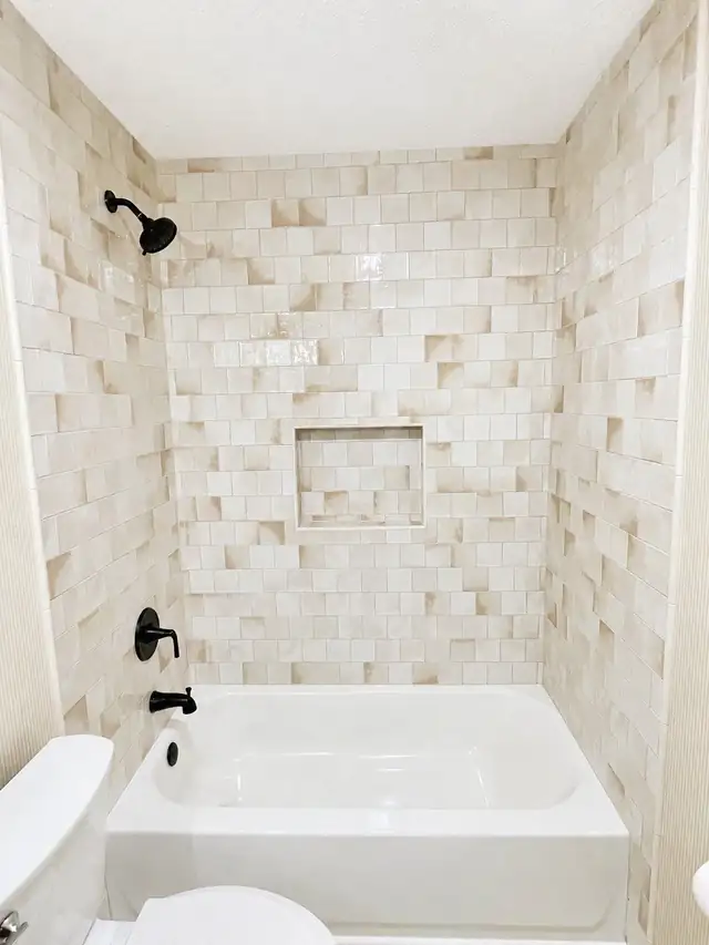 Tub surround in cream handmade-look tile with a centered niche and matte black shower fixtures
