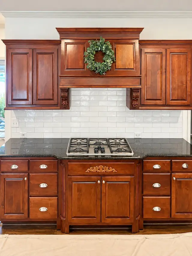 Glossy white subway tile backsplash between cherry kitchen cabinets and a black granite countertop with gas cooktop