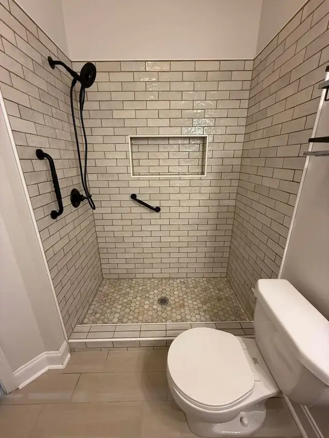 Walk-in shower in white subway tile with a recessed niche, hexagon mosaic floor, black fixtures and grab bars
